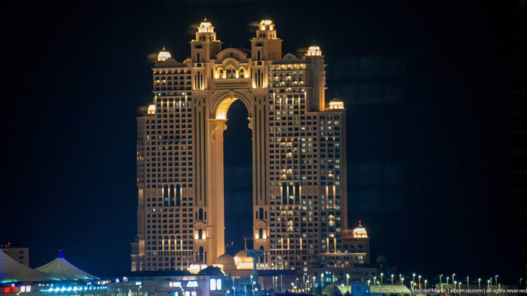 Night view of the Fairmont Marina Abu Dhabi hotel with a large central arch and warmly lit facade overlooking the waterfront.