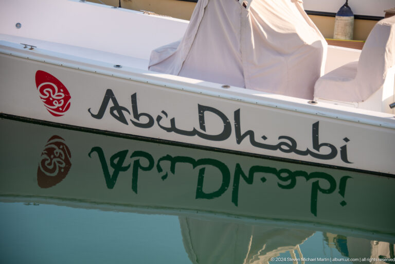 Close-up of a white boat hull branded with the word Abu Dhabi in English and Arabic beside colorful sponsor logos.