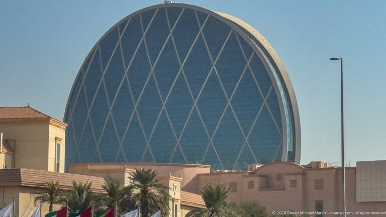 Daytime view of Etihad Arena on Yas Island, an oval building with a pale diamond-patterned exterior and low dome-like roof.