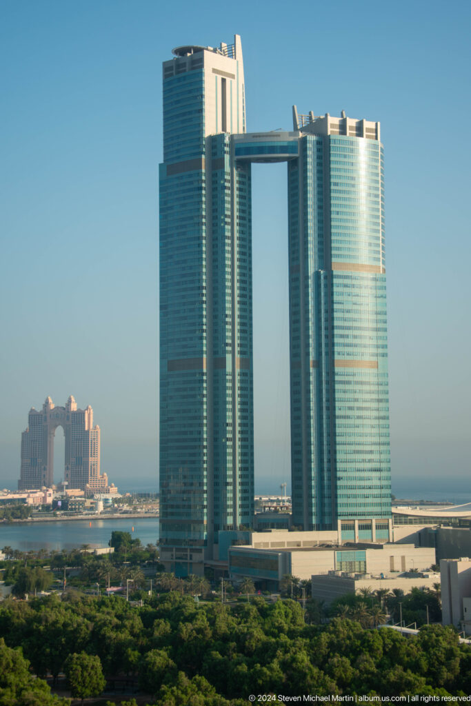 Telephoto view of Abu Dhabi skyline with curved glass Etihad Towers in the foreground and the ornate Fairmont Marina complex in the background.