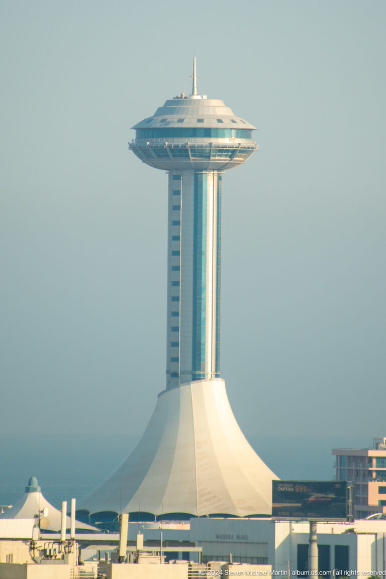 Telephoto view of the Marina Mall observation tower in Abu Dhabi, with a slender vertical shaft supporting a broad circular observation deck ringed by horizontal windows.