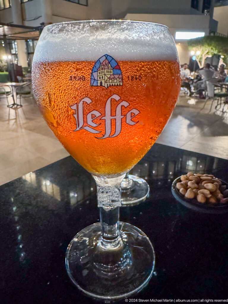 Close-up of a golden Leffe beer in a branded goblet on a table, with small snack bowls blurred in the background.