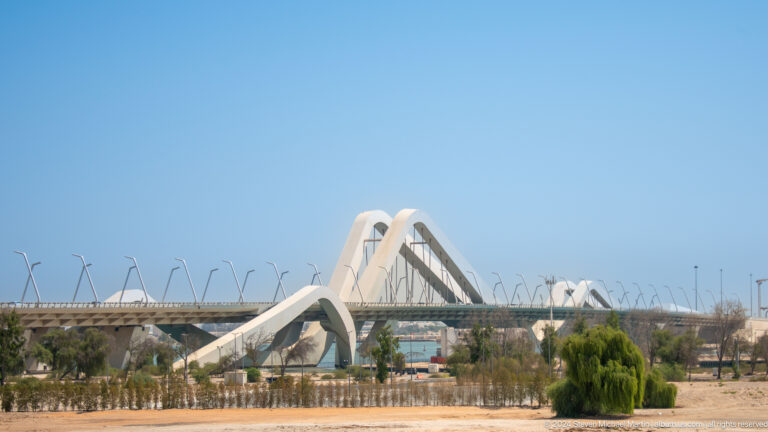Daytime view of Sheikh Zayed Bridge in Abu Dhabi, with white wave-like arches spanning the roadway above slender supports.