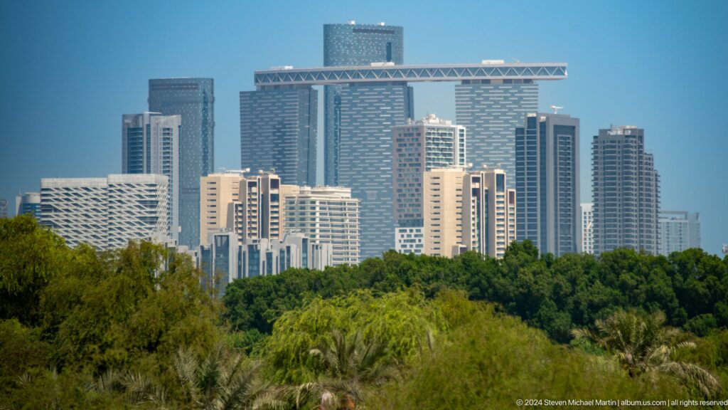 Telephoto view of Abu Dhabi’s skyline behind a wide expanse of dense green mangrove canopy along the coast.