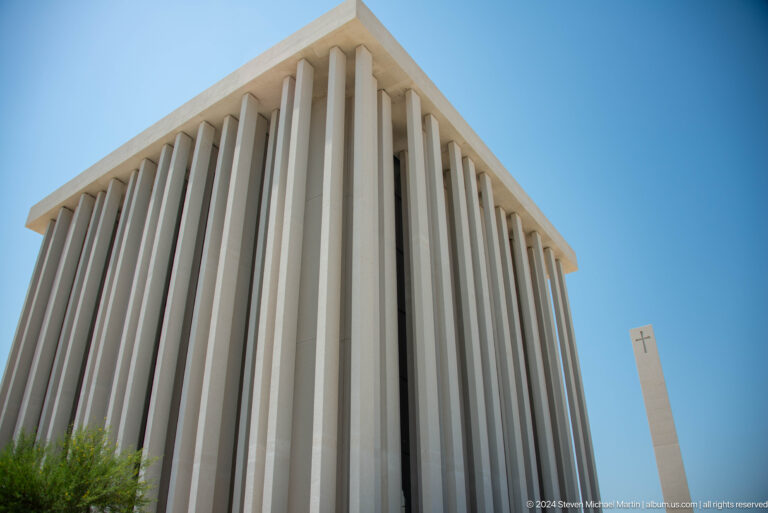 Low-angle view of a white cubic building in Abu Dhabi, its tall vertical fins casting strong linear shadows against a clear blue sky.