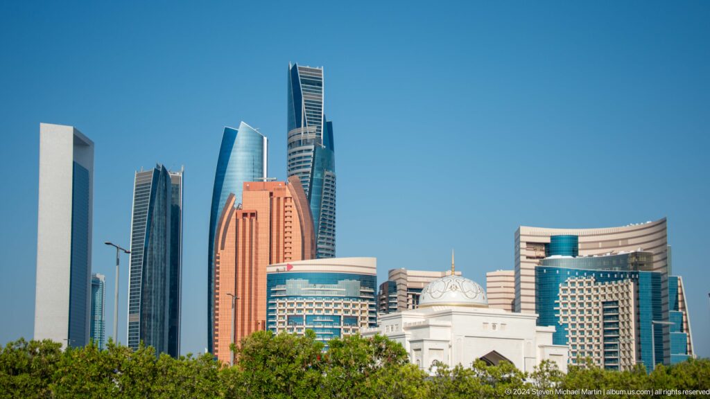 Daytime telephoto view of Abu Dhabi’s central skyline with modern high-rise towers rising behind lower white buildings in the foreground.