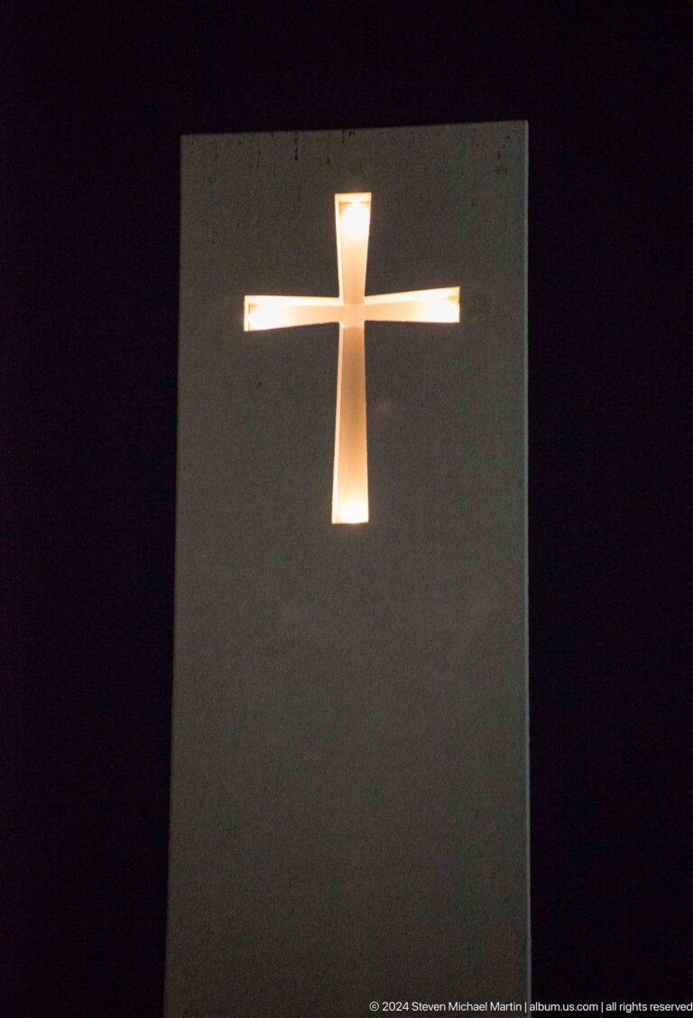 Illuminated Latin cross glowing against a plain dark wall inside St. Francis Church at the Abrahamic Family House.