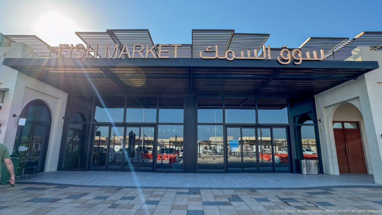 Frontal view of the Souq Al Mina Fish Market entrance in Abu Dhabi’s Mina Zayed district, with bilingual English and Arabic signage above a modern glass façade.