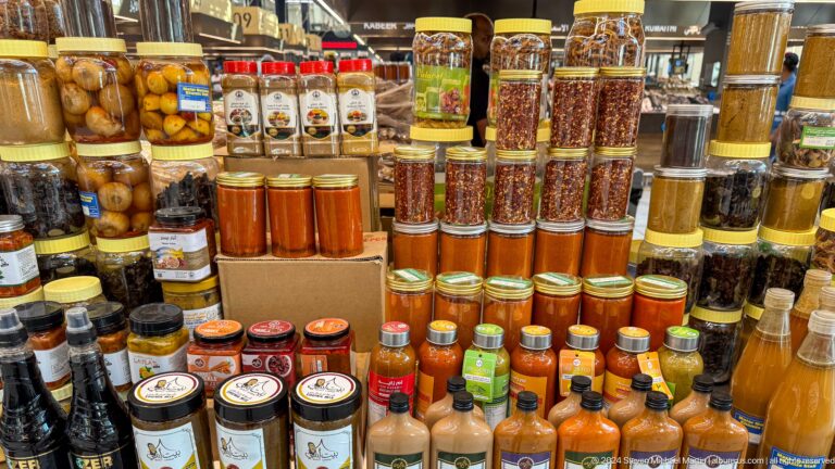 Tall shelves at Souq Al Mina lined with glass jars of spices, pickles, and preserved foods in dense vertical rows.