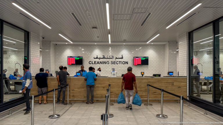 Interior of the cleaning section at Souq Al Mina Fish Market, showing customers waiting with bags at numbered service counters beneath a large bilingual CLEANING SECTION sign.