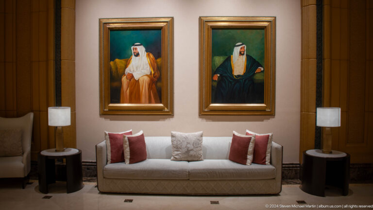 Symmetrical hotel lounge at Emirates Palace with a central sofa and two large framed portraits of Emirati leaders hanging on the wall above it.