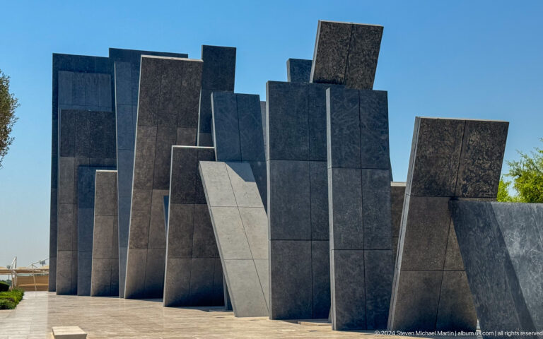 Close view of the overlapping dark stone tablets of Wahat Al Karama in Abu Dhabi, filling the frame with angled planes at differing heights.