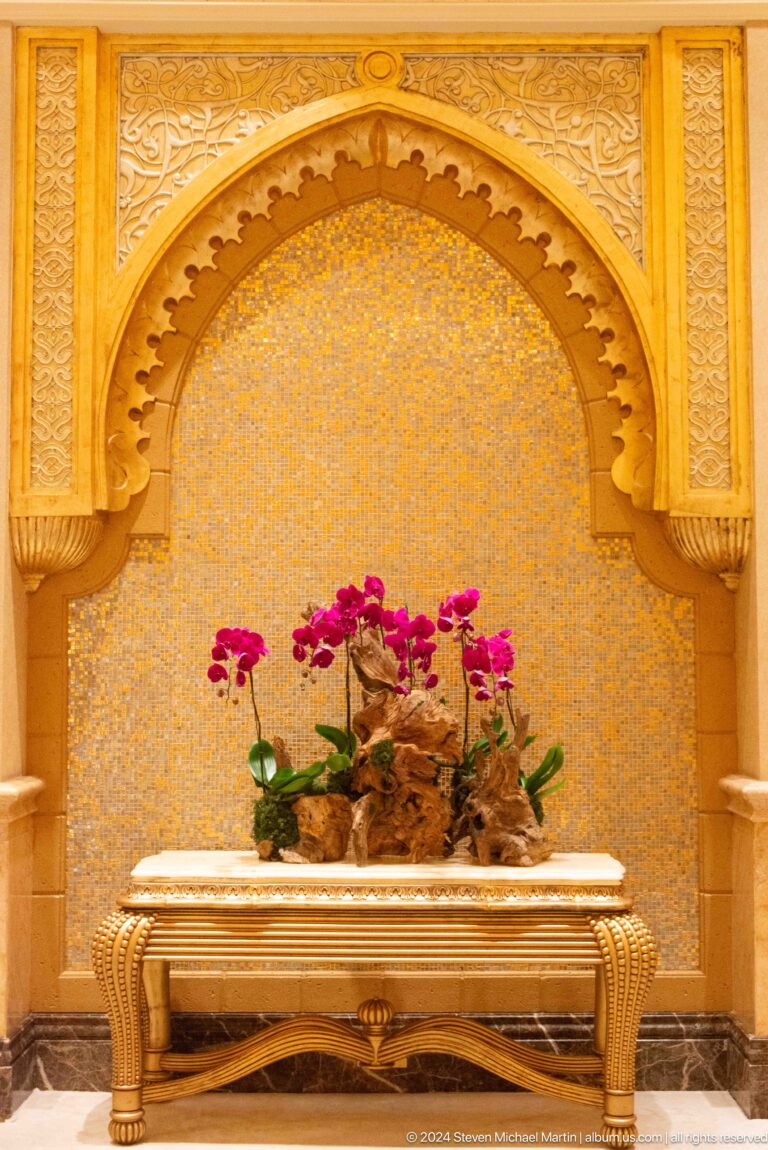 Magenta orchids in a dark planter set against an ornate gold-patterned wall and arched niche inside Emirates Palace.