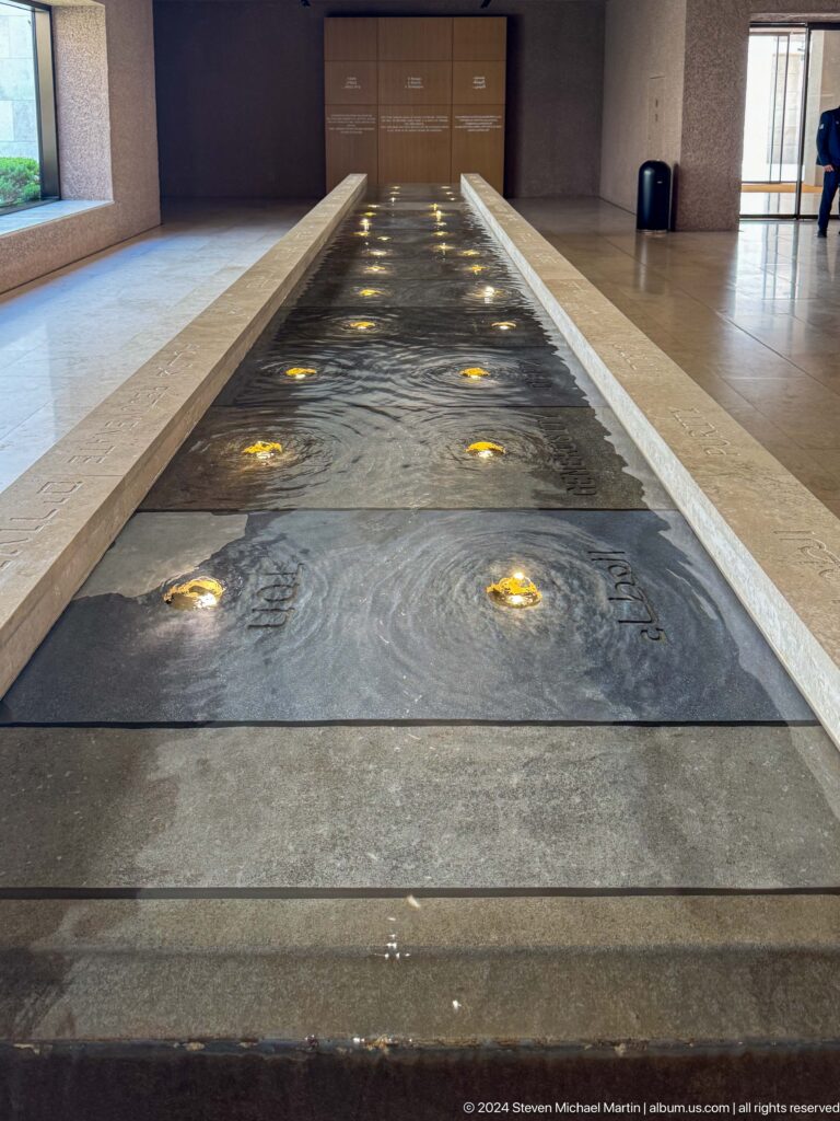 Close, low-angle view of The Founder's Memorial path in Abu Dhabi, showing a dark surface with repeating circular golden lights and subtle engraved patterns.