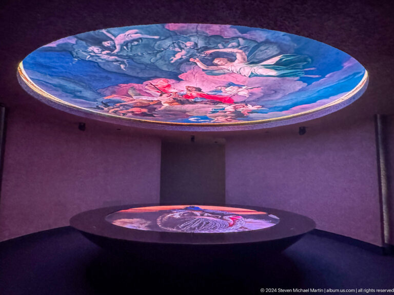 Dark gallery at the Abrahamic Family House with a large circular projection above a matching circular display below, both showing colorful religious or cultural imagery.