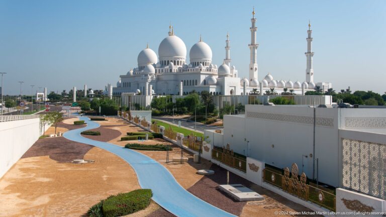 Elevated view of mosque domes and minarets beyond curving landscaped paths and blue channels.