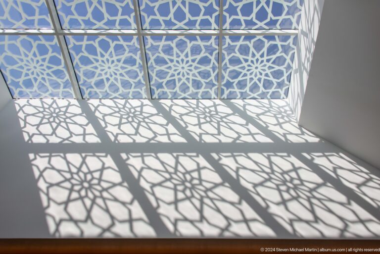 Geometric lattice shadows cast across a white floor and wall.