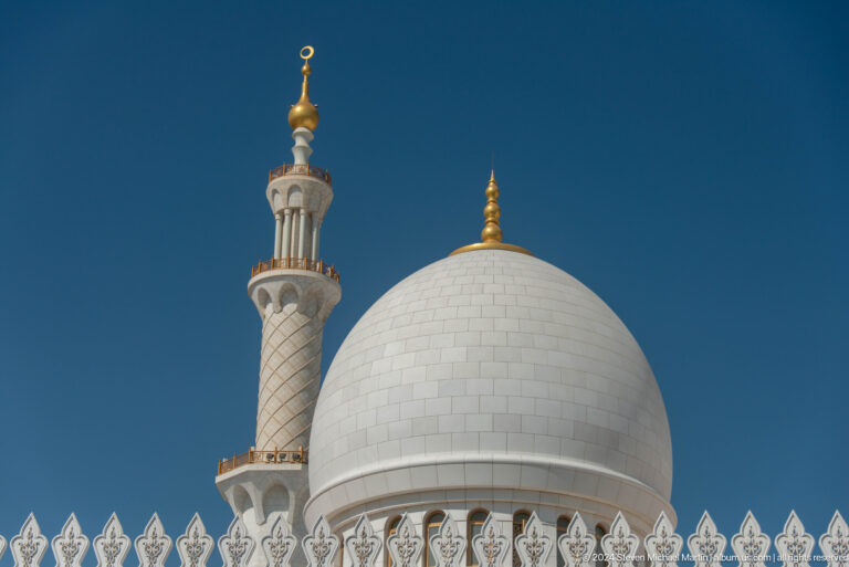 Large white dome and slender minaret with gold finials against blue sky.