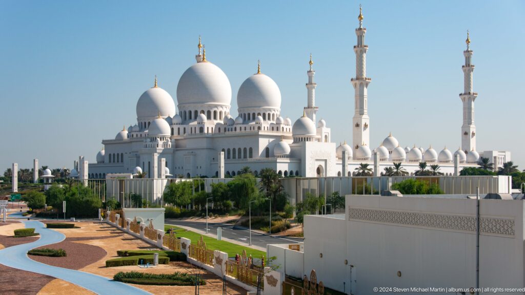 Elevated view of the mosque’s white domes and minarets above landscaped grounds.