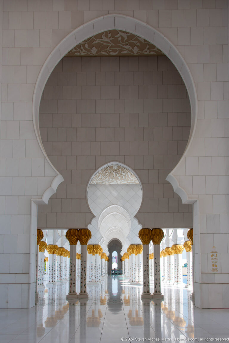 Layered white arches converging around a circular medallion with gold capitals below.