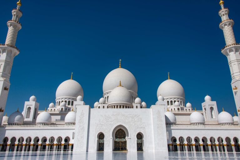 Central white domes and arched façade framed by partial minarets.