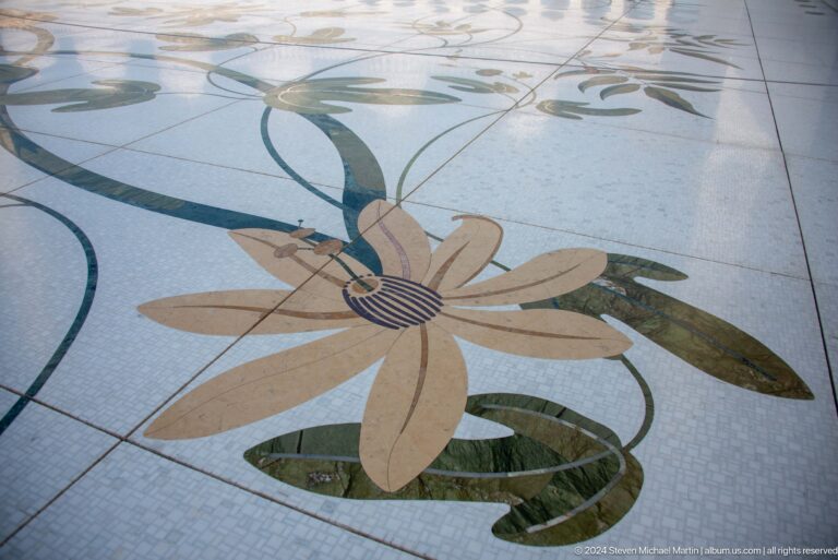 Large tan and green floral stone inlay set into pale courtyard paving.