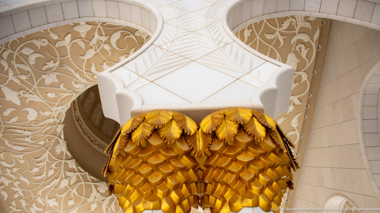 Gold palm-like column capital beneath a pale patterned ceiling.