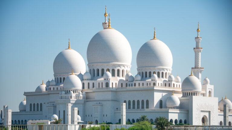 Three large white domes with gold finials above smaller domes and a minaret.