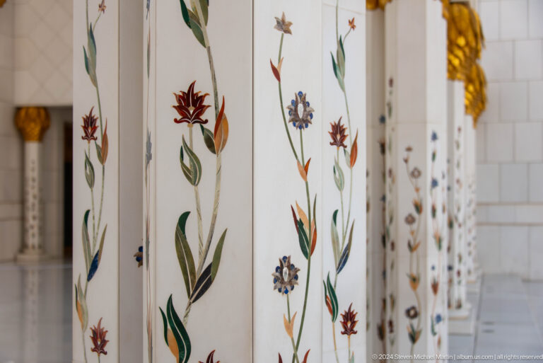 White marble columns with red and green floral stone inlay.