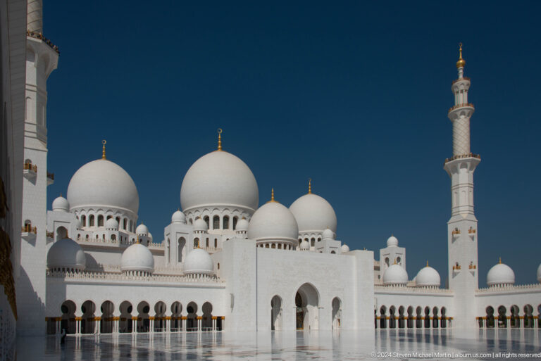 Clustered white domes and a minaret above the mosque courtyard façade.