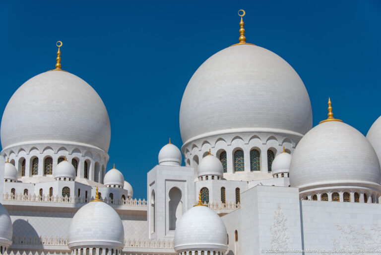 Large and small white domes with gold finials layered against blue sky.