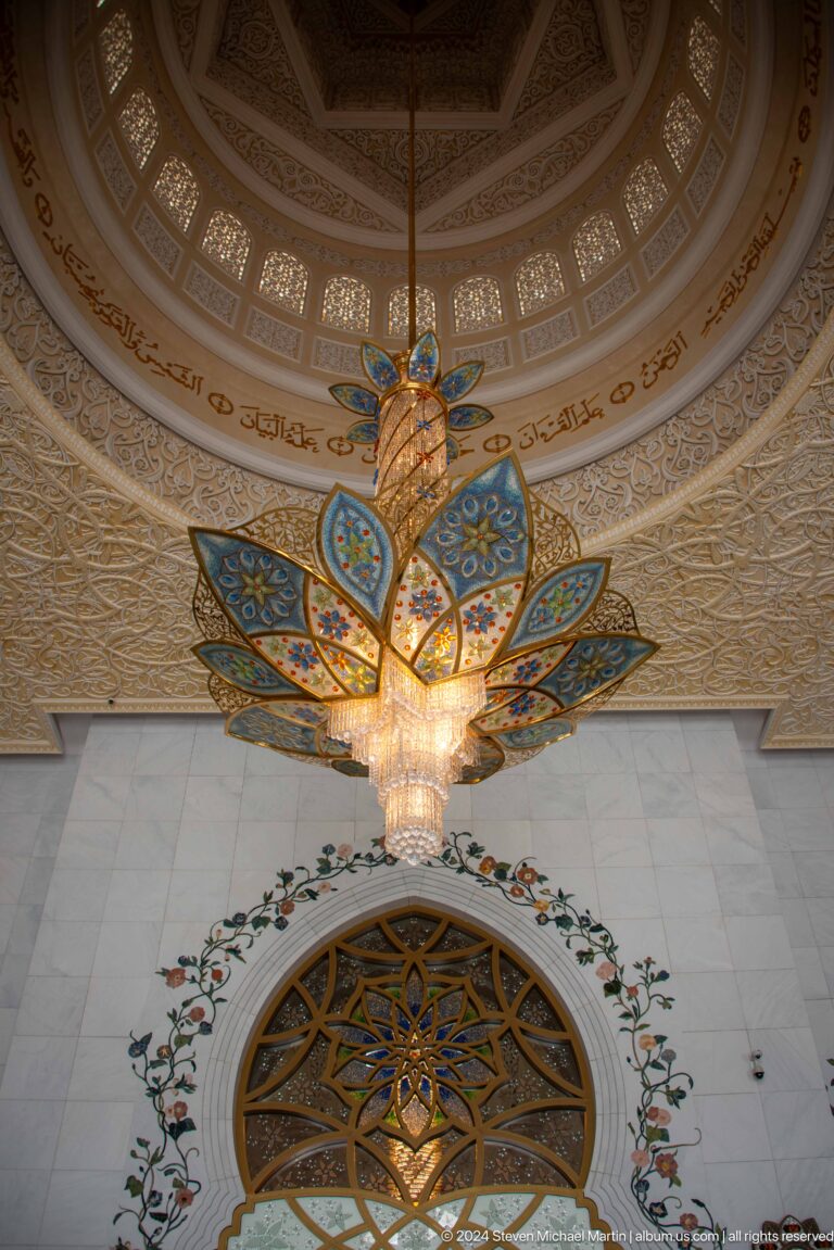 Blue-and-gold lotus-like chandelier with crystal center beneath an ornate ceiling.