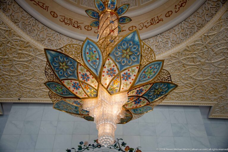 Centered blue-and-gold floral chandelier with crystal core against an ornate ceiling.