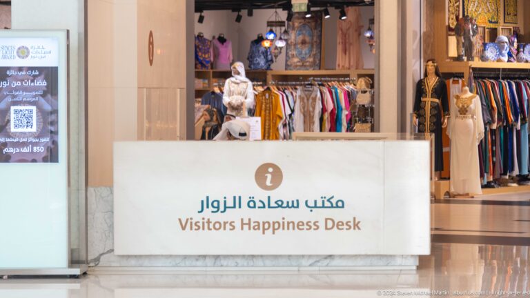 Visitor Happiness Desk with Arabic-English signage and merchandise displays behind the counter.