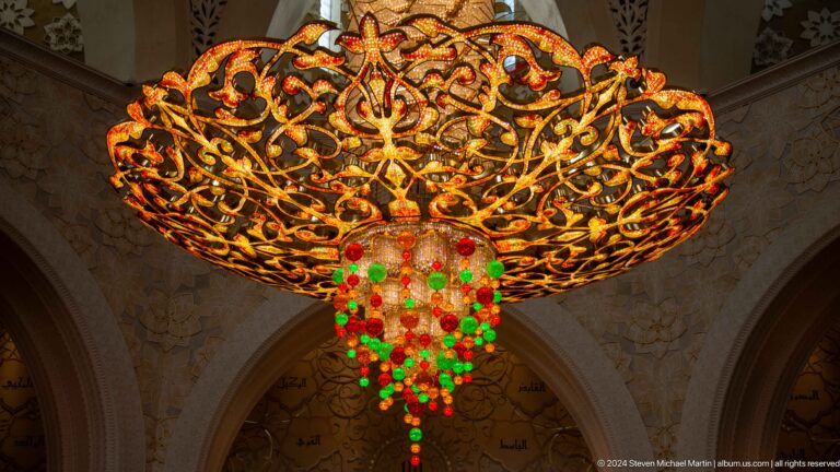 Close underside view of gold chandelier metalwork with red and green glass drops.