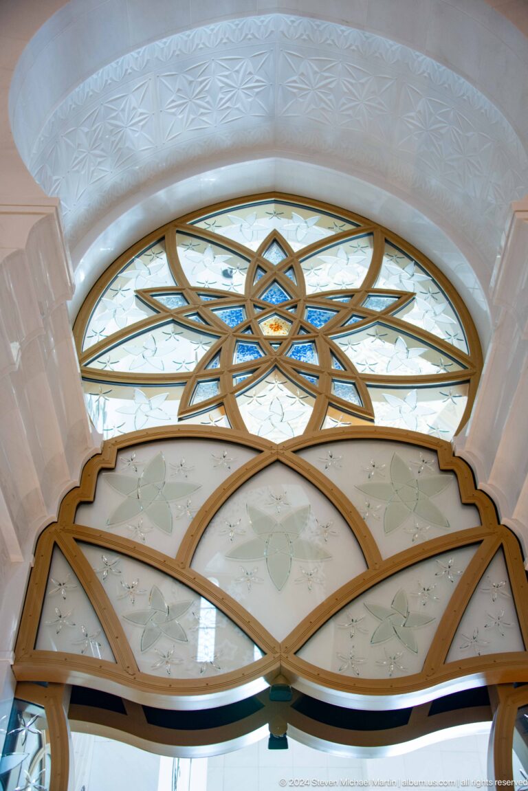 Arched window with a gold-toned interlaced star over pale floral glass and blue accents.