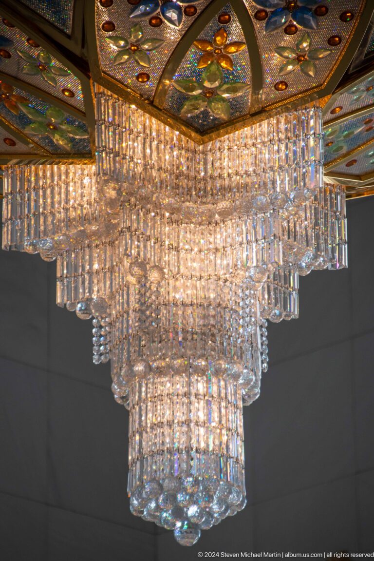 Tiered cascade of clear crystal rods, prisms, and droplets sparkling against a dark background.