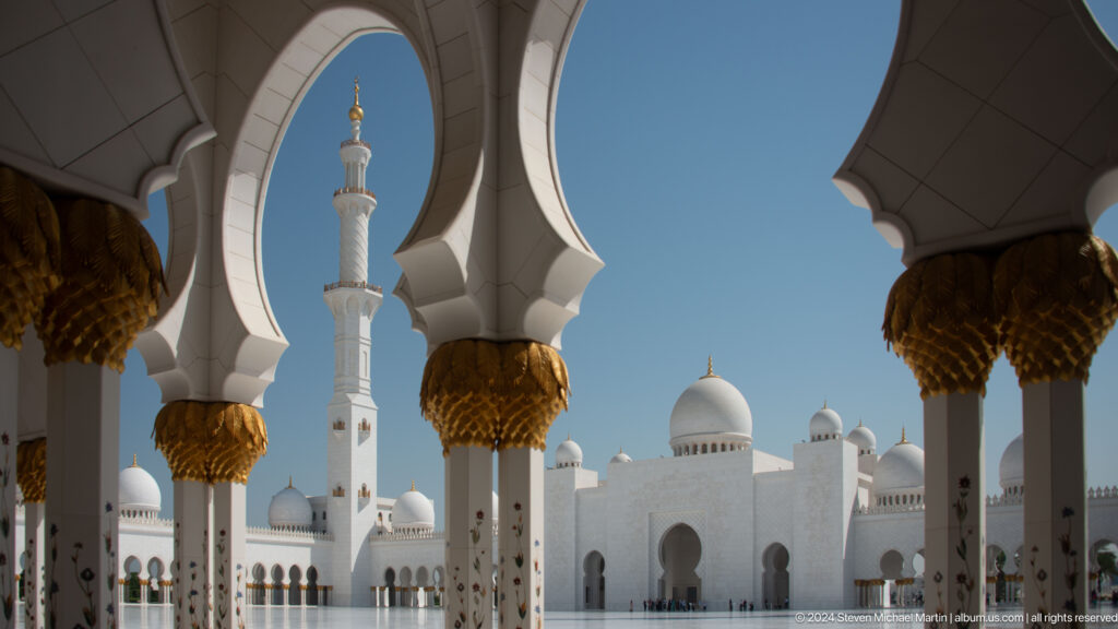 Scalloped courtyard arches and gold-topped columns frame a white minaret and domes.