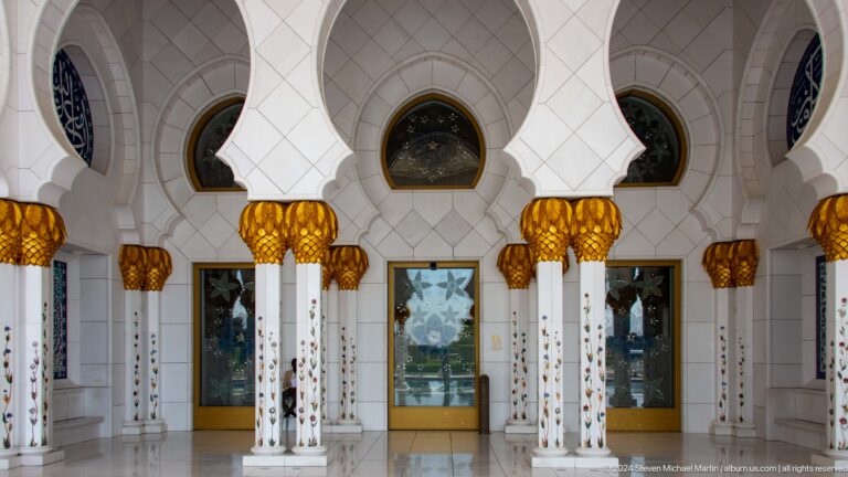 Three white arched entrance bays with floral columns, gold capitals, and reflective glass doors.