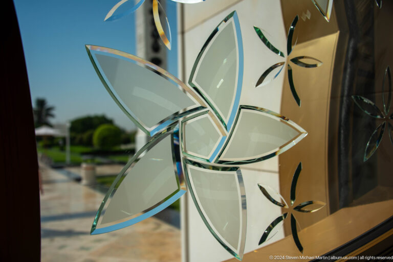 Close-up of a translucent glass panel etched with a pale blue flower and green stems.