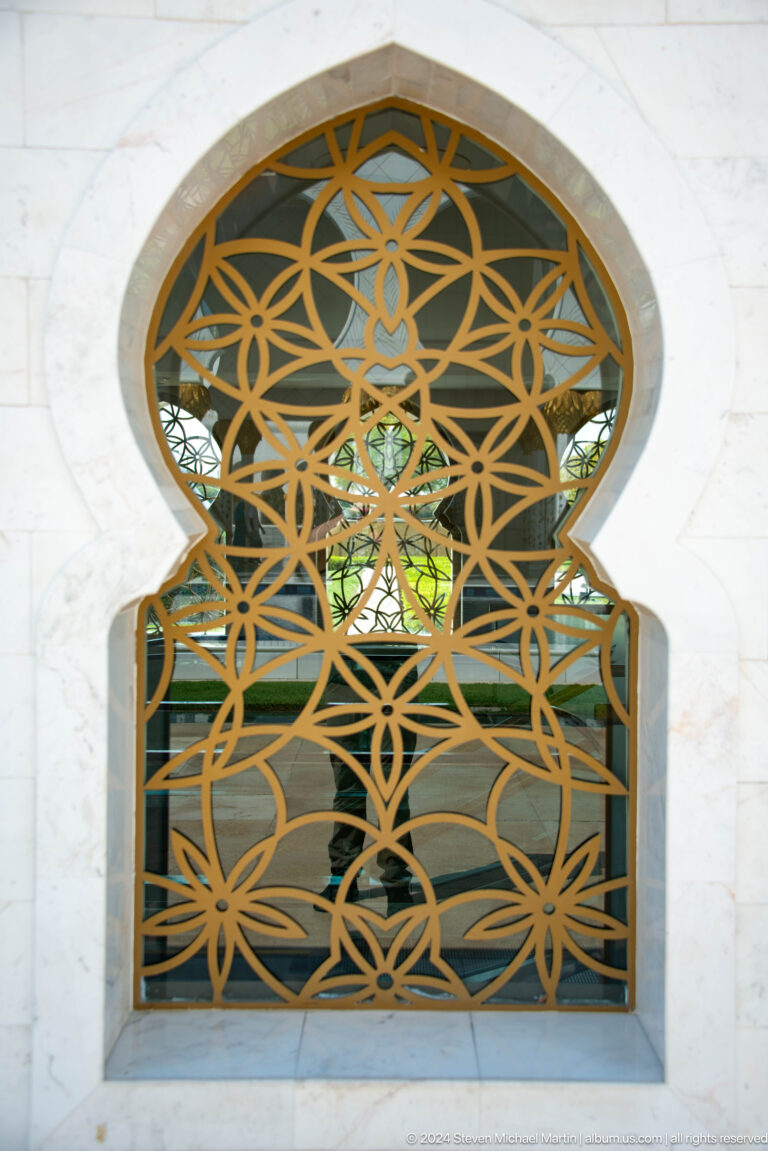 Gold interlaced geometric lattice filling a keyhole-shaped opening in white marble.