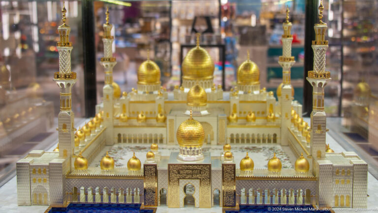 Miniature mosque model with gold domes and towers displayed behind glass.