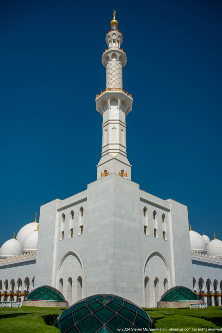 Square white tower base and lower minaret stage rising against a deep blue sky.