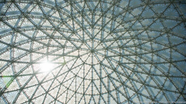 Sunburst shining through a radial grid of metal framing and triangular glass panels.