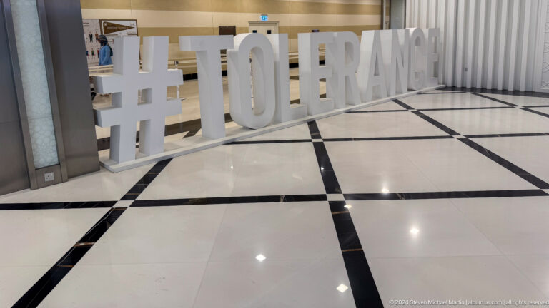 Large white '#TOLERANCE' sign on a polished black-and-white floor inside a visitor area.