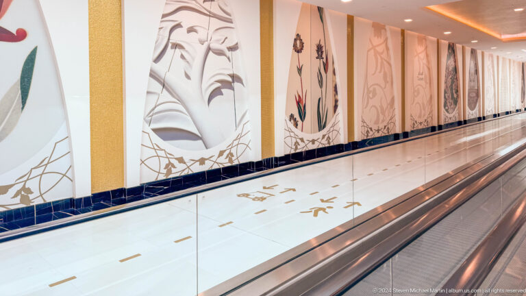 Moving walkway in a long corridor lined with illuminated floral panels and polished flooring.