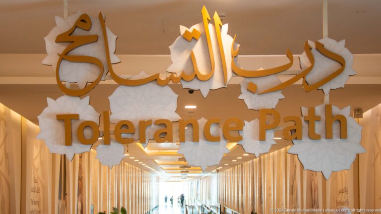 Gold Arabic calligraphy above the English words Tolerance Path on a beige wall.