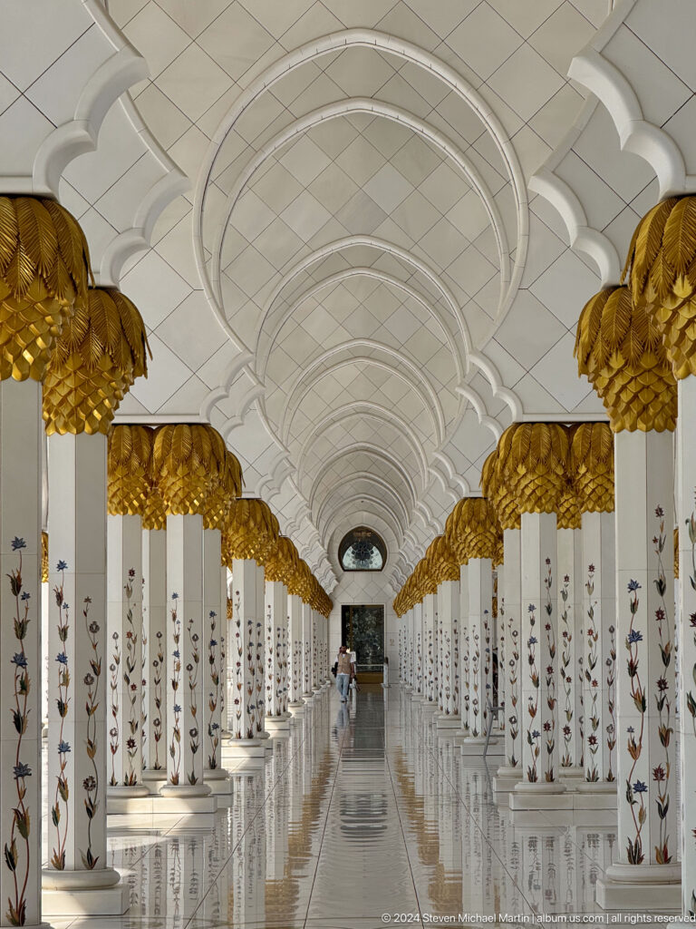 Centered colonnade with white floral-inlaid columns, gold palm capitals, and repeating vaulted arches.