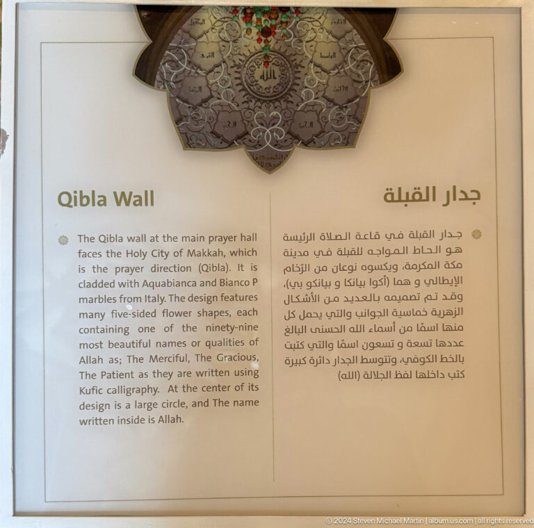 Bilingual panel titled 'Qibla Wall' with English and Arabic explanatory text and an ornamental plaque above.