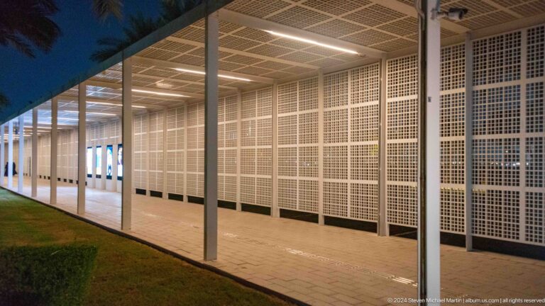Illuminated colonnade with white lattice wall at Louvre Abu Dhabi.